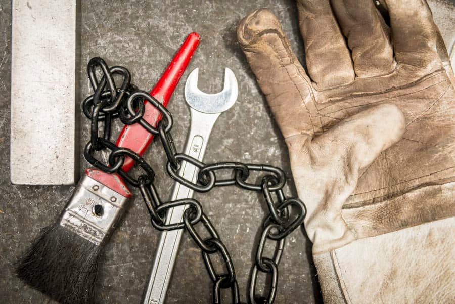 A pair of gloves, a wrench, and a chain on a concrete surface.