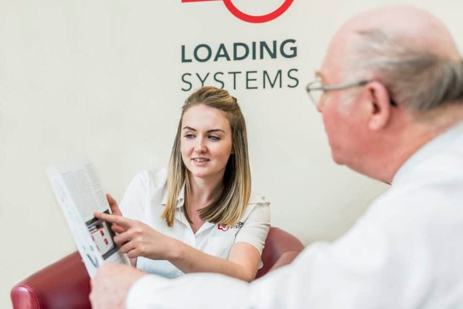 A man and woman sitting in a chair talking about loading systems.