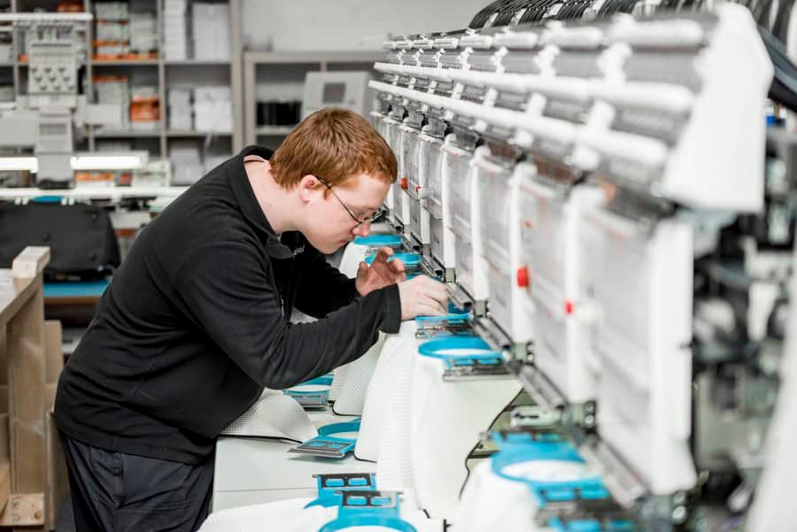 A man working on an embroidery machine in a factory.