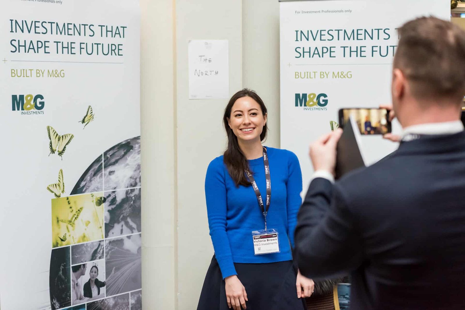 A woman is taking a picture with a sign that says investing investments that shape the future.