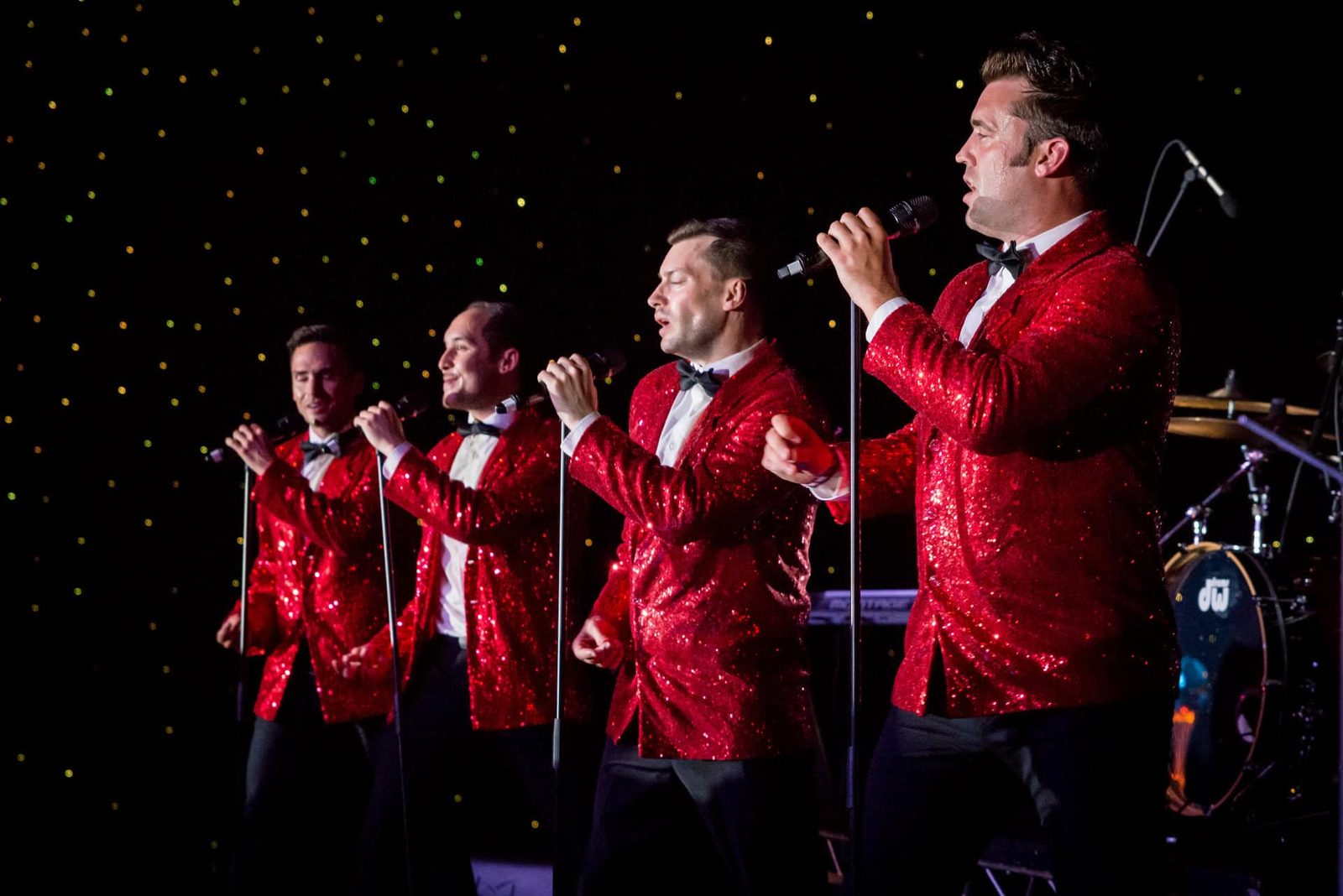 A group of men in red tuxedos singing into microphones.