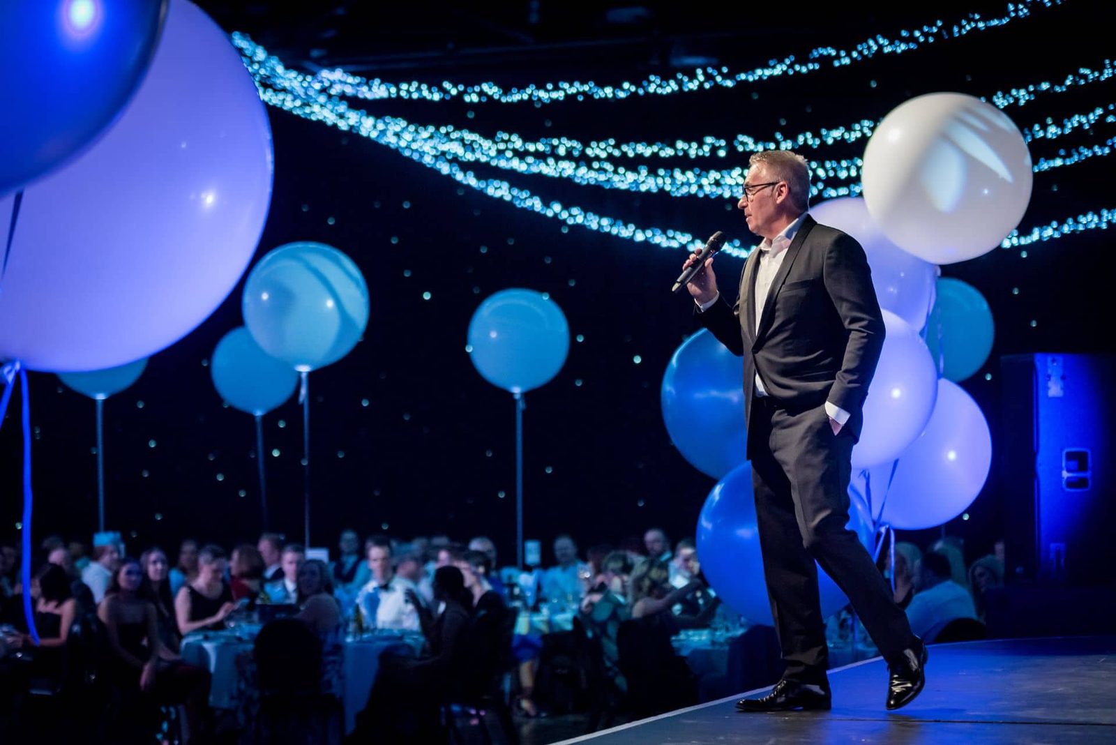 A man in a suit standing in front of balloons.