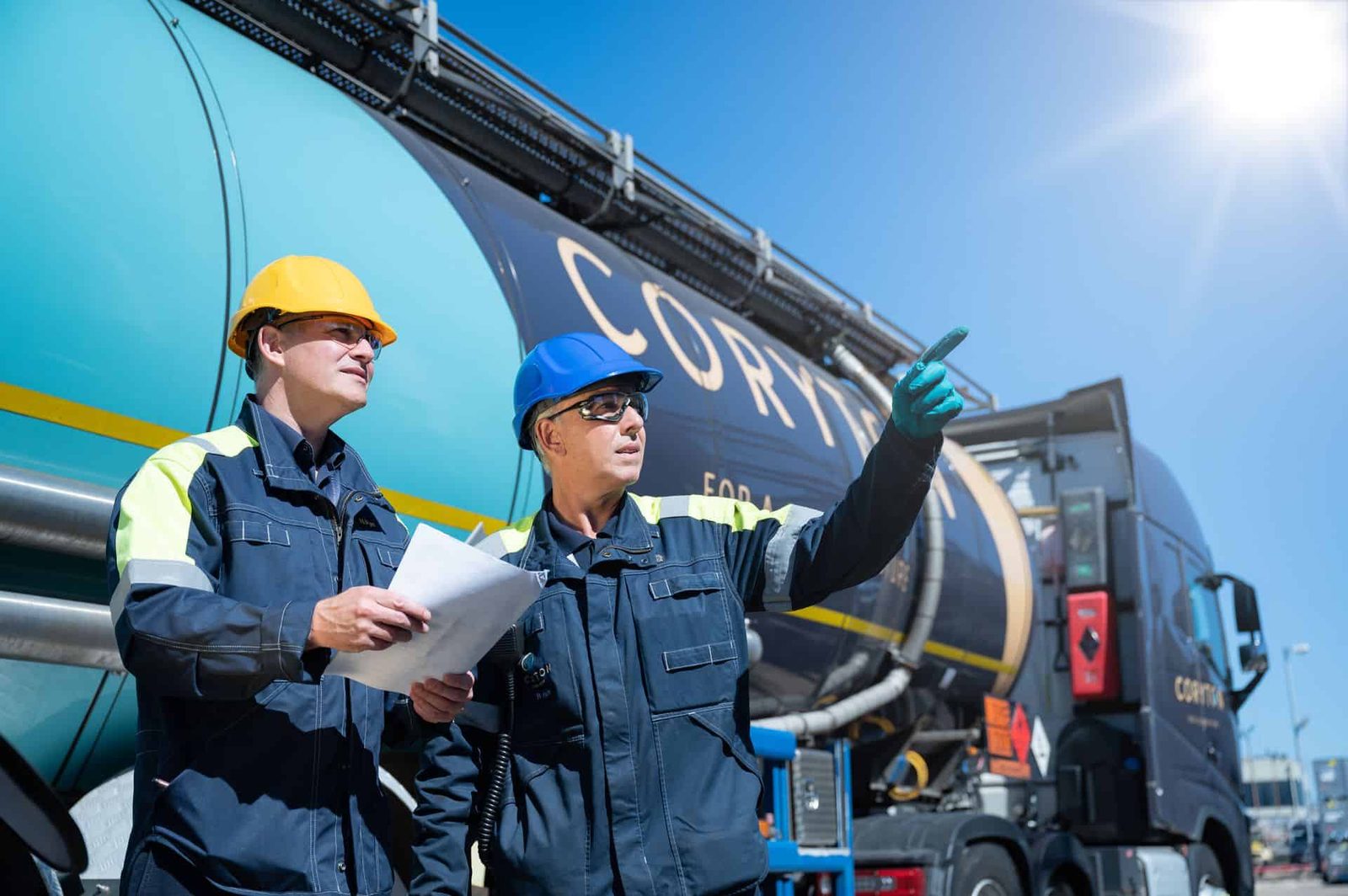 Two men in hard hats standing next to a large truck.