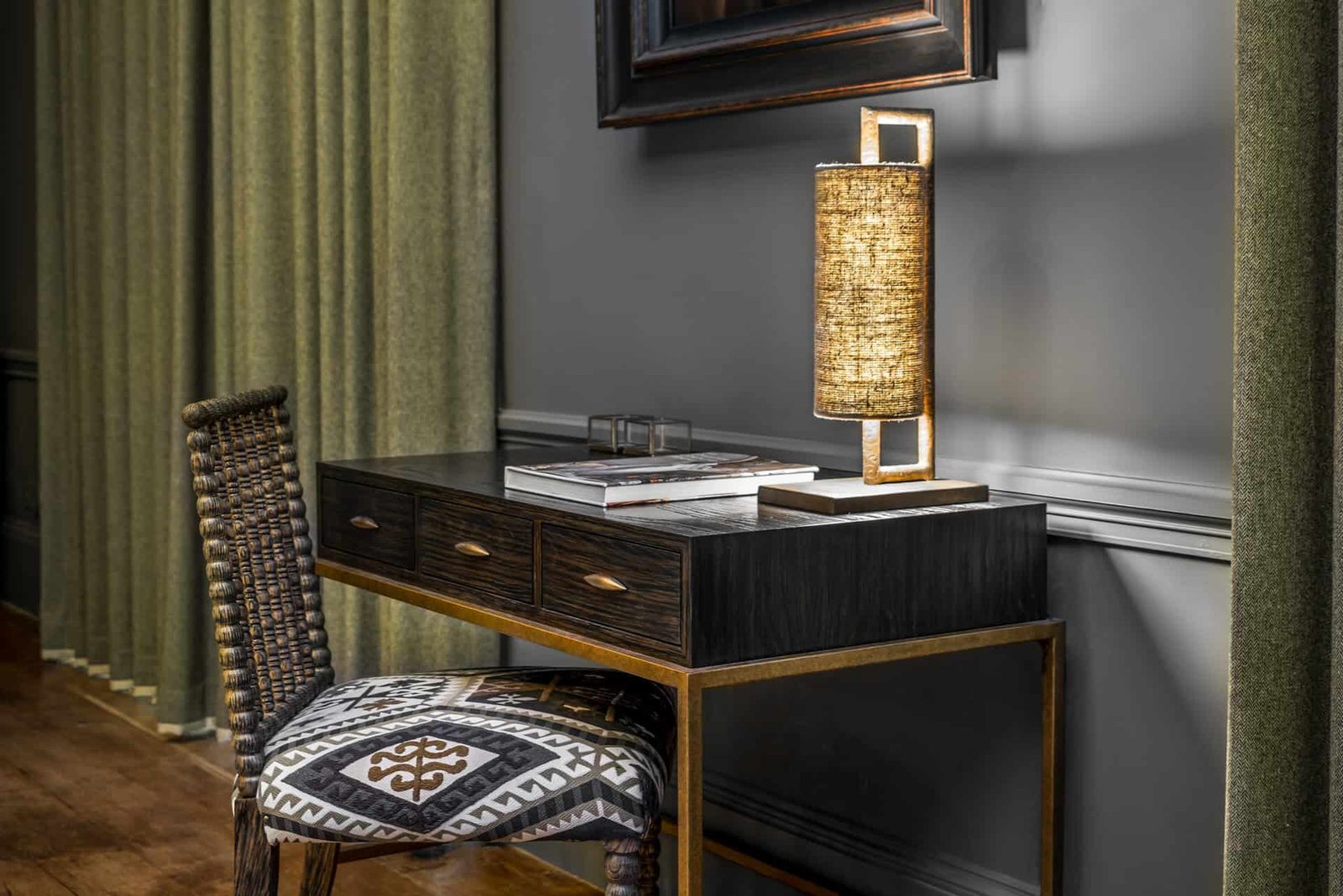 A desk in a room with green curtains and a lamp.