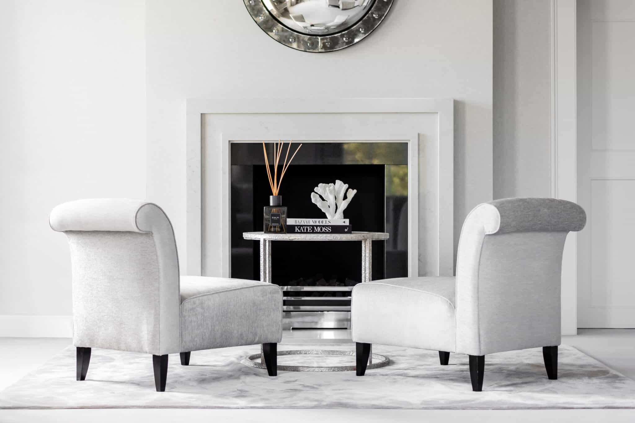 A pair of grey velvet chairs in front of a fireplace.