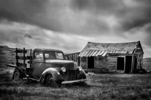 A black and white photograph of an old truck and a barn.