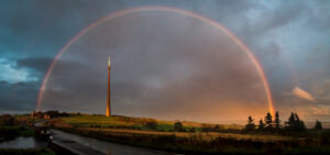 A rainbow over a hill with a tower in the background.
