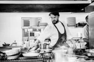 A black and white photo of a man cooking in a kitchen.