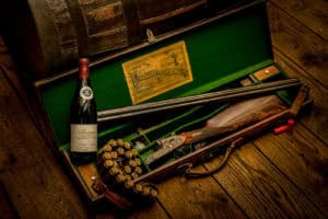 A wooden trunk with a bottle of wine and a gun.