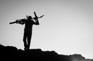 A silhouette of a man carrying a bike on top of a mountain.