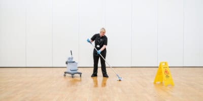 A woman cleaning a wooden floor with a mop.