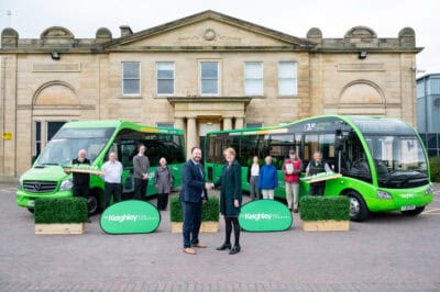 A group of people standing in front of green buses.