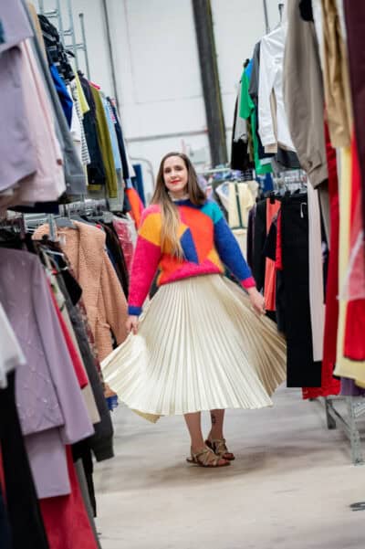 A woman in a skirt walking through a rack of clothes.