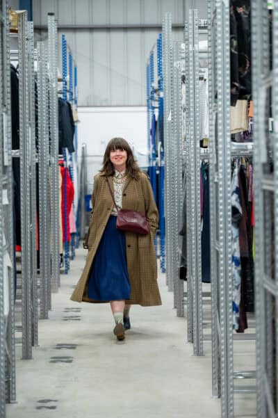 A woman walking through a warehouse full of clothes.