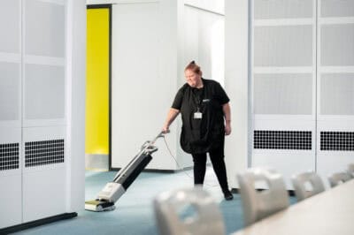 A woman cleaning a hallway with a vacuum cleaner.