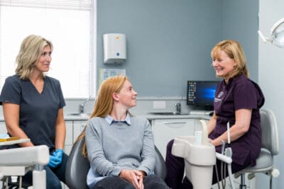 Three women sitting in a dental chair talking to each other.