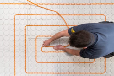 A man working on a tile floor with an orange cord.