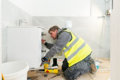 A man in a yellow vest working on a bathroom.