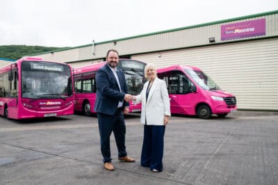 Two people shaking hands in front of pink buses.