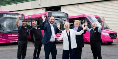 A group of people standing in front of a pink bus.