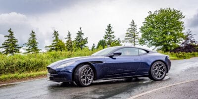 The blue aston martin db9 is driving down the road.