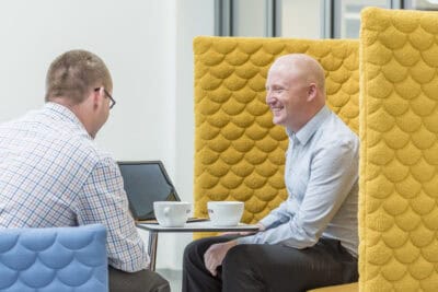 Two men sitting in a yellow chair talking to each other.