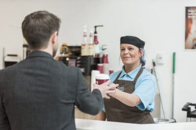 A man is shaking hands with a woman at a coffee shop.