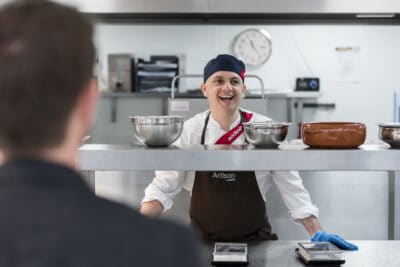 A woman in a chef's hat is standing in front of a kitchen.