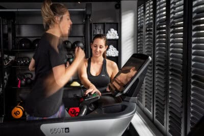 Two women working out on a tread machine in a gym.