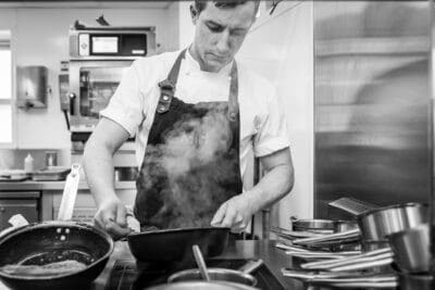 A black and white photo of a chef cooking in a kitchen.