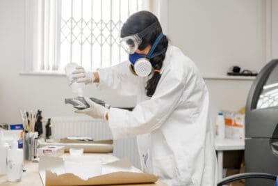 A woman wearing a lab coat and goggles working in a lab.