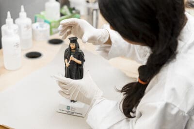 A woman in a lab coat is working on a figurine.