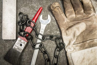 A pair of gloves, a wrench, and a chain on a concrete surface.
