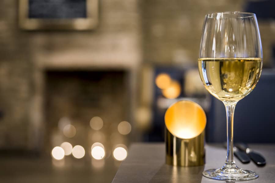 A glass of white wine sits on a table in front of a fireplace.