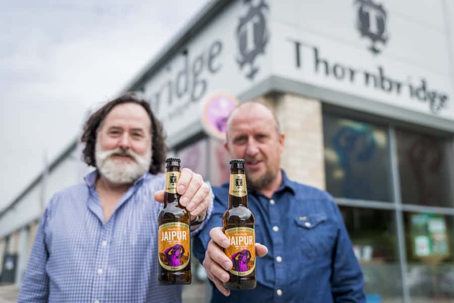 Two men holding up bottles of beer in front of a store.