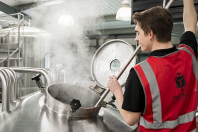 A man in a red vest working in a brewery.