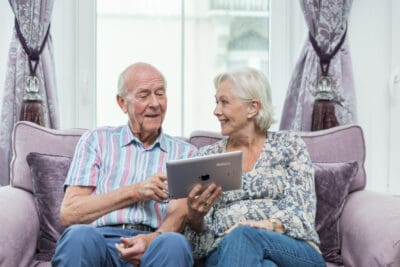 An elderly couple sitting on a couch using a tablet computer.