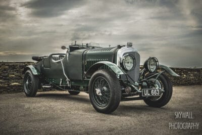 An old green bentley parked in front of a stone wall.