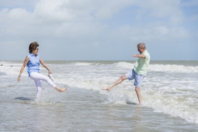 An older couple kicking a ball in the ocean.
