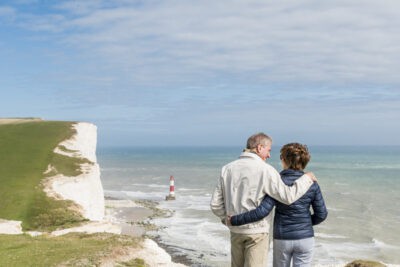 A man and woman standing on a cliff overlooking the ocean.