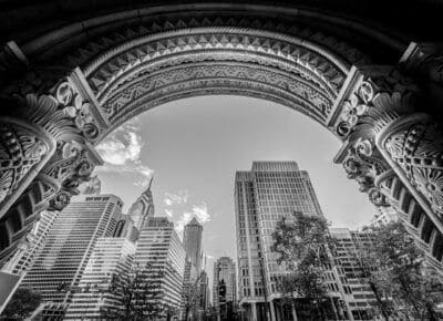 A black and white photo of an arch in the middle of a city.