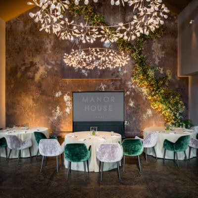 A room set up for an event with green chairs and chandeliers.