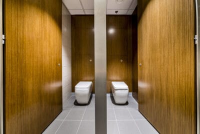 Two toilets in a bathroom with wooden doors.