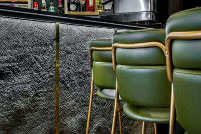A bar with green leather chairs and a black wall.