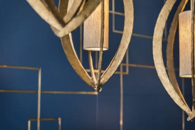 A pair of gold chandeliers hanging on a blue wall.
