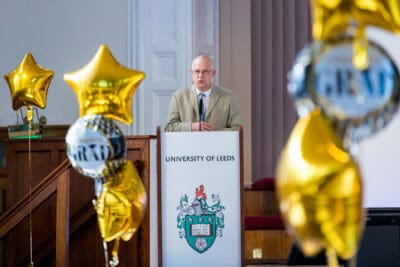 A man standing at a podium with gold balloons.