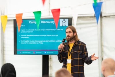 A man giving a presentation in front of a tent.