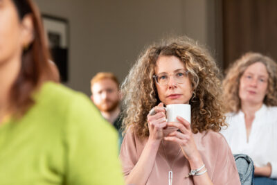 A group of people sitting in a room with a woman holding a cup of coffee.
