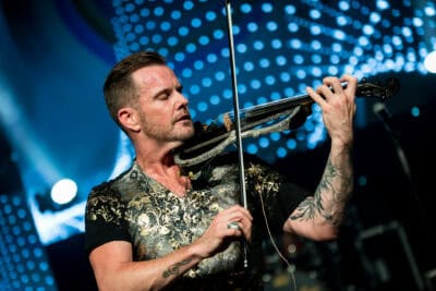 A man with tattoos playing a violin on stage.