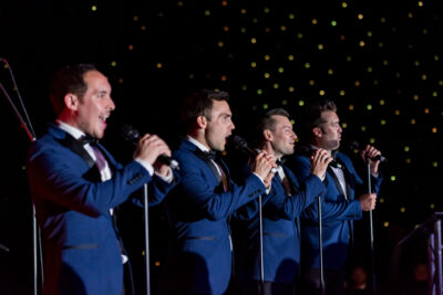Four men in tuxedos singing into microphones.